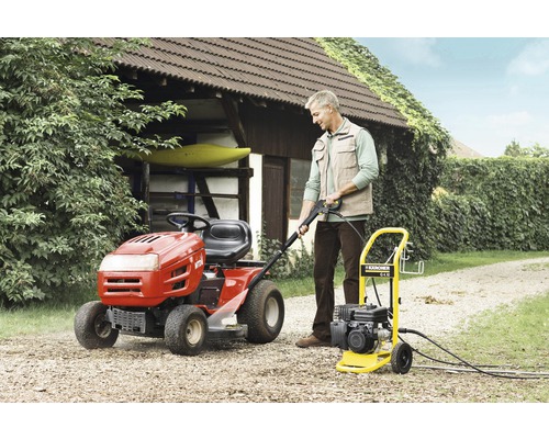 En man använder en Kärcher högtryckstvätt bredvid en trädgårdstraktor i trädgården.