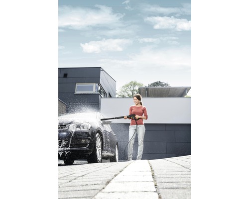 Kvinna rengör bil med högtryckstvätt framför ett hus.