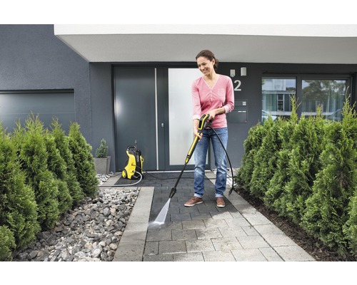 Kvinna använder högtryckstvätt för att rengöra en trottoar framför huset