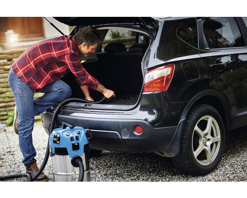 En man dammsuger bagageutrymmet på en bil med en våt- och torrdammsugare.