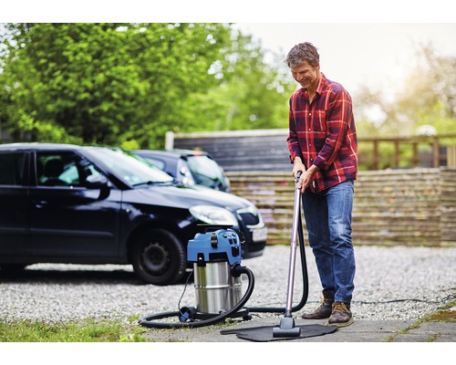 Man dammsuger en bilmatta med en våt- och torrdammsugare framför en bil.