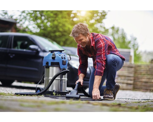 Man använder en rengöringsdammsugare för att rengöra insidan av en bil utomhus.
