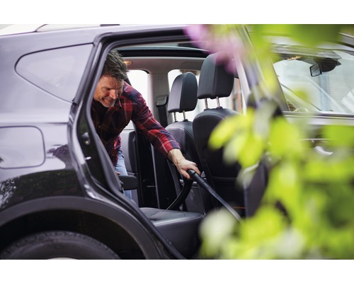 Man dammsuger insidan av en bil med en dammsugare