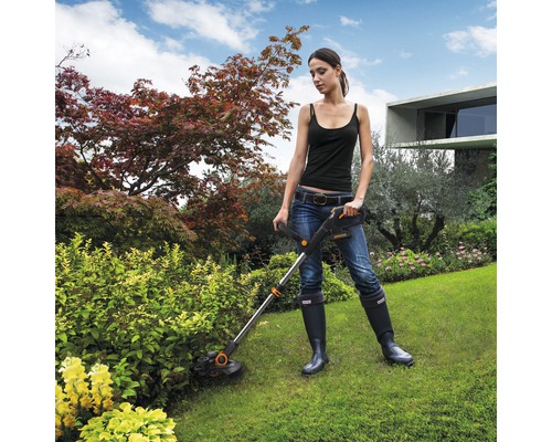 Kvinna använder en grästrimmer i trädgården.