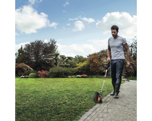 En man använder en gräskantstrimmer i trädgården för att trimma gräsmattan.