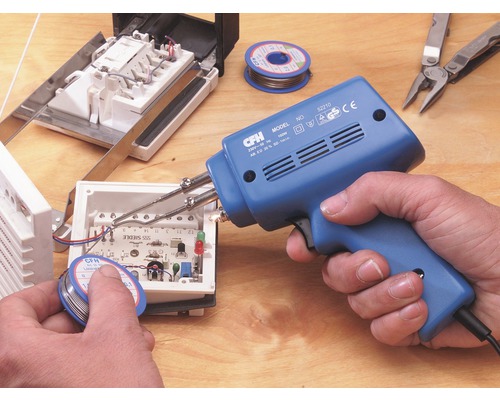 En person använder en lödpistol för att löda elektroniska komponenter i ett hölje. Loddtin, multiverktyg och andra elektroniska komponenter ligger på ett bord.