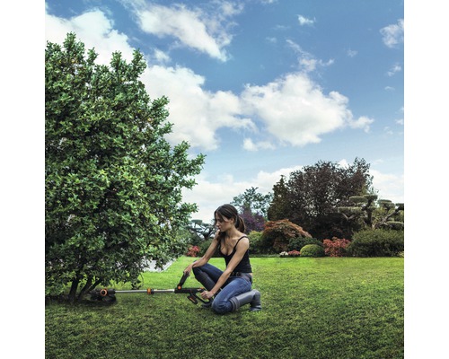 Kvinna arbetar med en batteridriven grästrimmer i trädgården vid ett träd