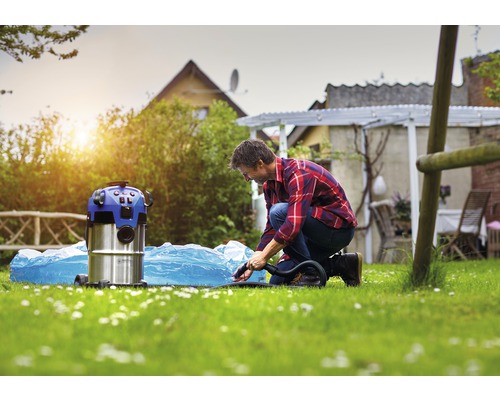 En man använder en våt- och torrdammsugare för att rengöra en pool som ligger i trädgården.