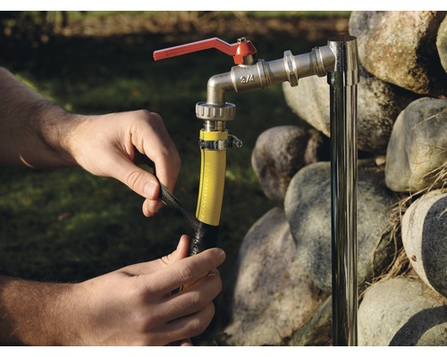 En person lindar isoleringstejp runt en trädgårdsslang som är ansluten till en vattenkran.