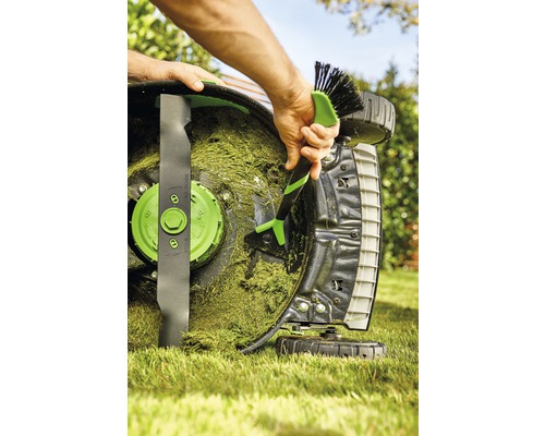 En person rengör en gräsklippare med en borste för att ta bort gräsrester.
