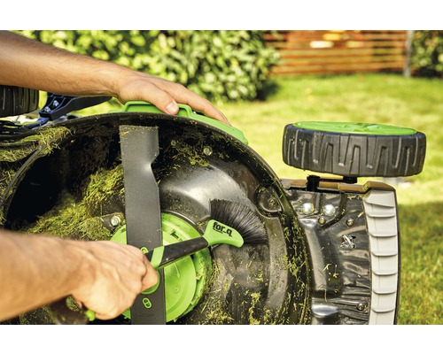 En person rengör en gräsklippare med en borste.