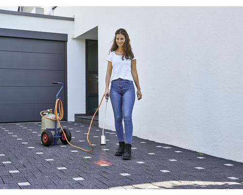 Kvinna använder en gasbrännare för att bekämpa ogräs på en stenlagd uppfart framför ett hus med garage