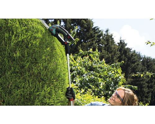Kvinna klipper häck med en batteridriven teleskopisk häcksax