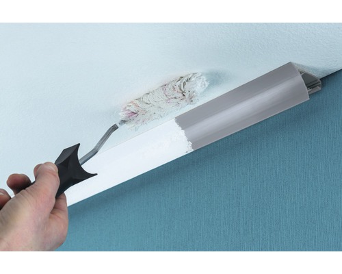 En person målar en dekorlist med en färgroller i ett tak.