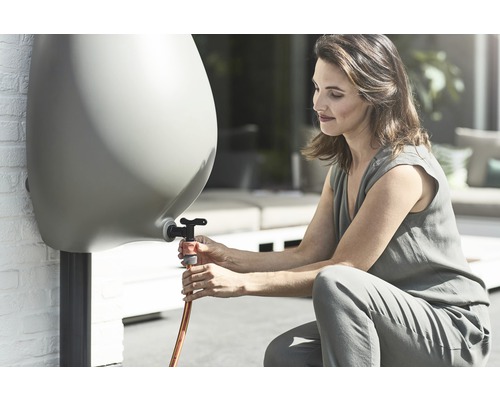 Kvinna ansluter en trädgårdsslang till en regntunna i trädgården.