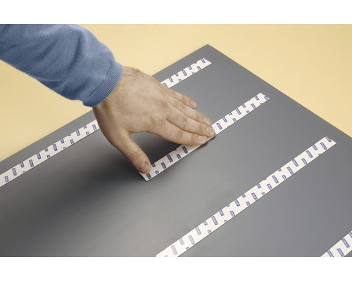 Hand applicerar dubbelsidig tejp på en platta.