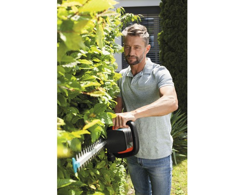 Man klipper en häck med en häcksax i trädgården.