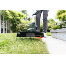 Person klipper gräs med en grästrimmer i trädgården.