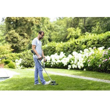 En man trimmar gräsmattan i en trädgård med en grästrimmer.