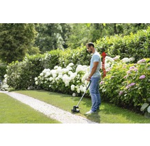 Man klipper gräs med en grästrimmer i trädgården.