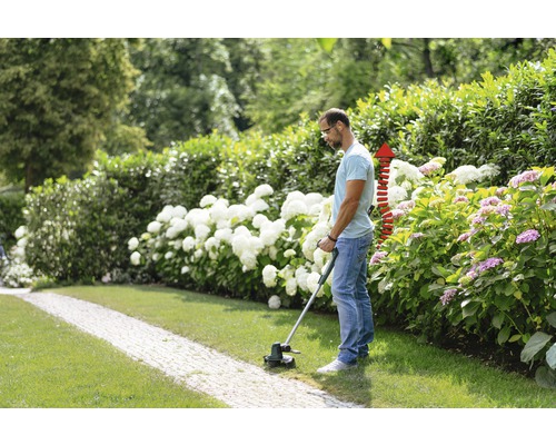 Man klipper gräs med en grästrimmer i trädgården.