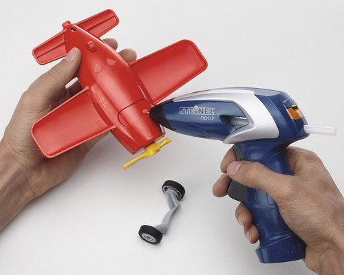 Person använder limpistol för att reparera en röd leksaksflygplan