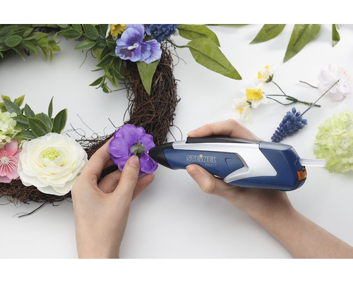 Kvinna fäster dekorationer med limpistol på en krans