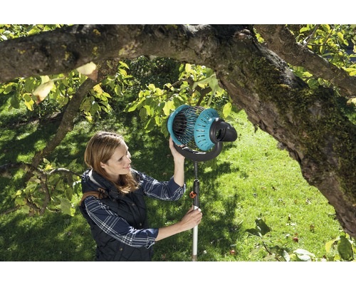 Kvinna använder fruktplockare i trädgården under ett träd.