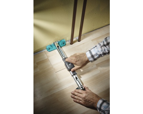 Person lägger laminat med ett dragjärn längs en vägg.