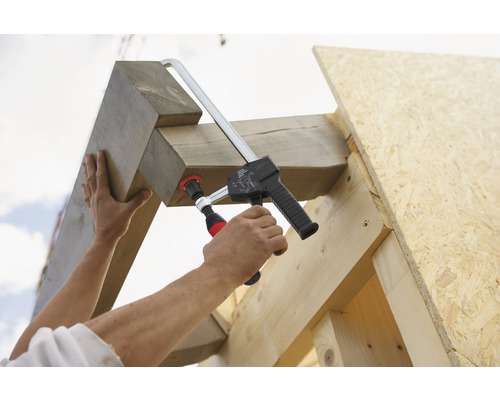 En person fäster träbjälkar på en träram med en skruvtving.