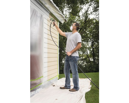 Man målar husvägg med färgspruta