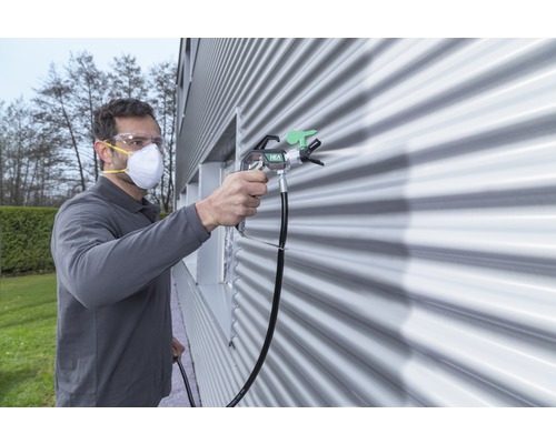 Man med skyddsglasögon och mask som sprutmålar en vägg med en färgspruta