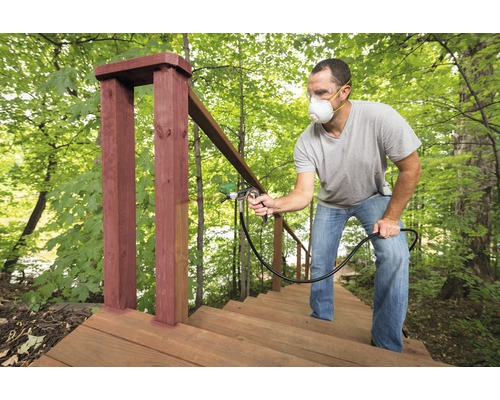 Man målar trätrappa utomhus med en färgspruta