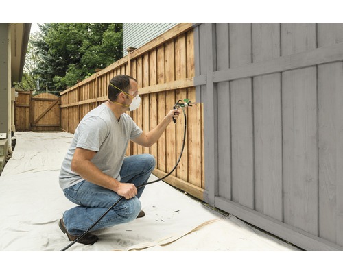 En person målar ett trästaket med en färgsprutpistol.