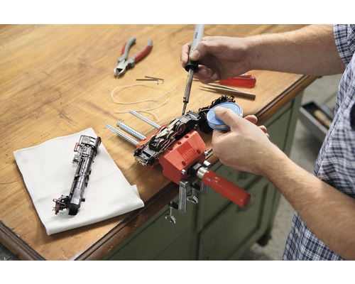 En person reparerar ett modelljärnväg med en lödkolv och en skruvtving