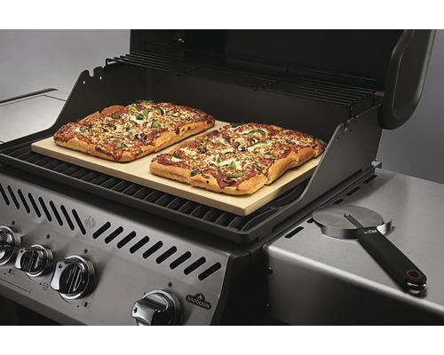 Gasolgrill med två pizzor på en pizzasten och en pizzaskärare.