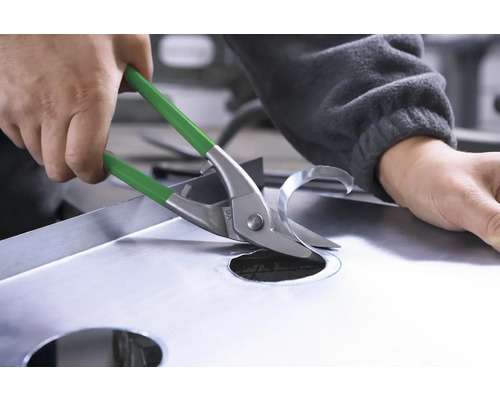 En person klipper ett hål i en metallplåt med en plåtsax.