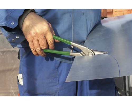 Hantverkare skär metallplåt med plåtsax