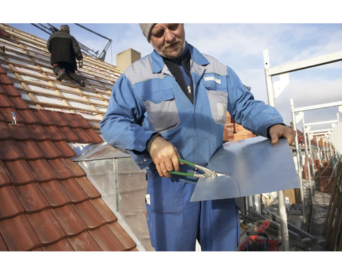 En hantverkare skär en plåtdel på ett tak med takpannor.