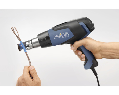 En hand håller en varmluftspistol och värmer en kabel.