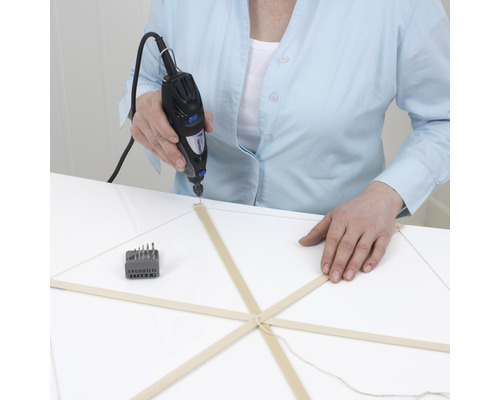 En person borrar ett hål i en träpinne med ett Dremel multifunktionsverktyg.