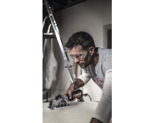 En man med skyddsglasögon sågar ett arbetsstycke med en cirkelsåg. En stege står i bakgrunden.