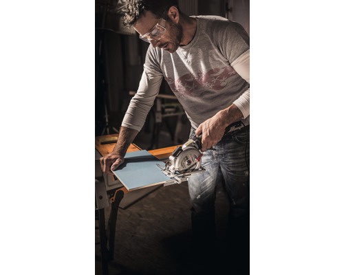 En man med skyddsglasögon skär en kakelplatta med en handsåg.