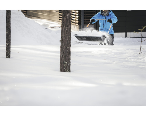 En person skottar snö med en snöskyffel framför ett hus.