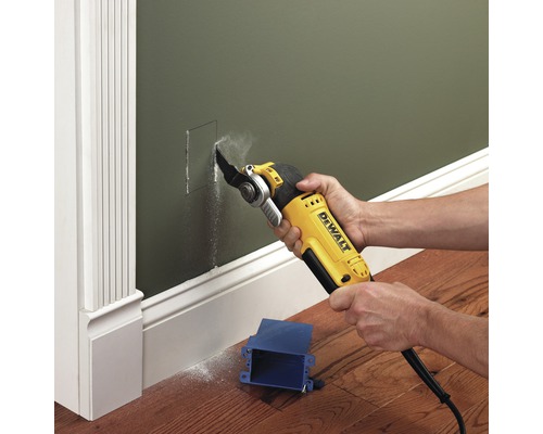 Oscillerande elverktyg skär ett hål i en grön vägg för en blå kopplingsdosa.