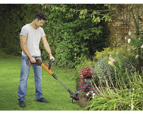 En man använder en batteridriven grästrimmer av märket Black and Decker i trädgården.