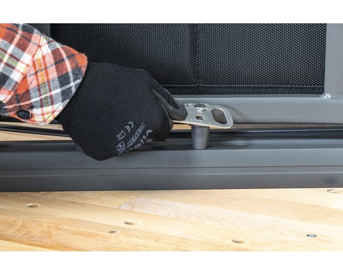 En person fäster ett silverfärgat metallfäste på ett fönstergaller.