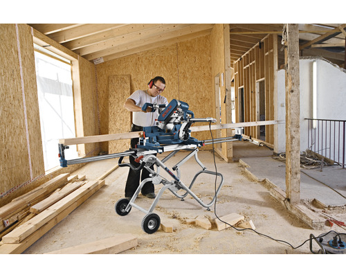 En person använder en Bosch kap- och gersåg på ett monteringsstativ i ett oavslutat rum.