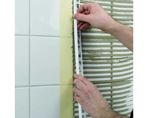 En man fäster en kakelskena på en vägg med kakel.