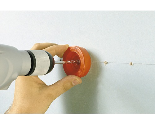 En person borrar ett hål i en vägg med en borrmaskin och ett dammskydd.